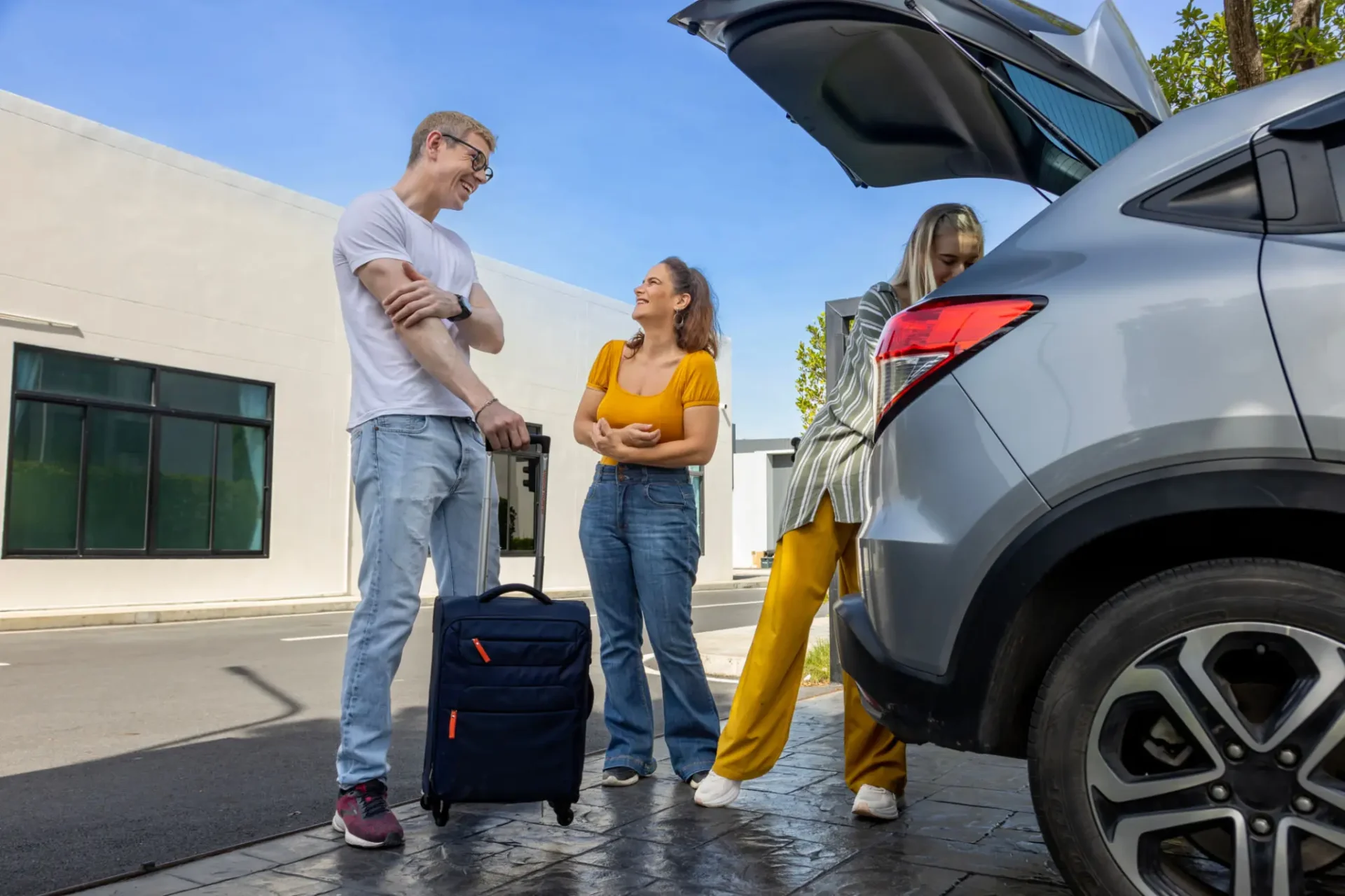 Friends loading luggage into car trunk